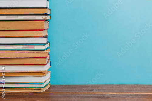 A simple composition of many hardback books, raw books on a wooden table and a bright blue background. Going back to school. Copy space. Education.