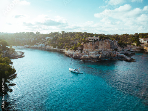 Drone panoramic image moored yachts on bright blue bay Cala Blanca Andratx, Palma de Mallorca, rocky coast breathtaking view, Balearic Islands Spain.