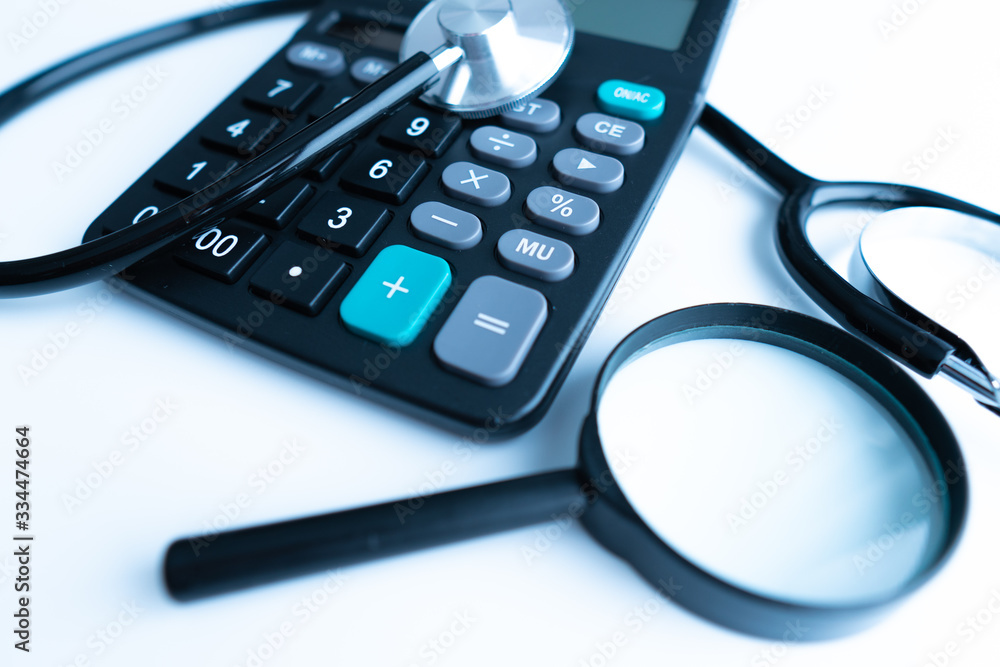 Concept of medical expenses or medical insurance for blog title and header. Stethoscope,white calculator and magnifying glass on wooden background. Concept of medical expenses or medical insurance for blog title and header. Stethoscope,white calculator and magnifying glass on wooden background.