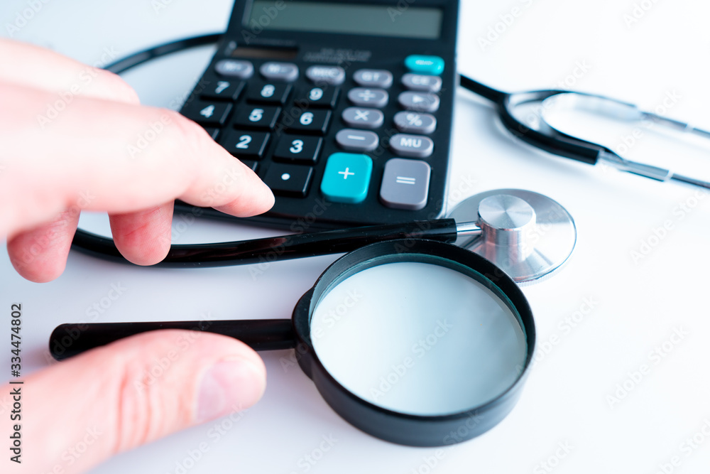 Selective focus Health care concept. Stethoscope on a calculator with Magnifying glass with effect light added. Selective focus Health care concept. Stethoscope on a calculator with Magnifying glass with effect light added.