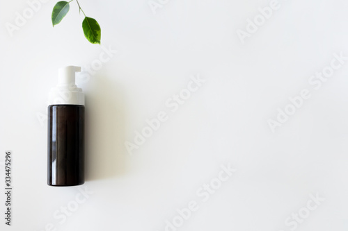 Cleanser foam in brown container with dispenser and fresh green leaves on white background witn copy space. Concept natural bio organic cosmetic  above