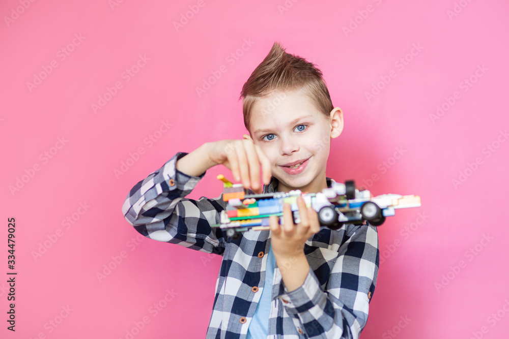 Baby, boy on a pink background plays plane robot made of designer on a pink background Baby, boy on a pink background plays plane robot made of designer on a pink background