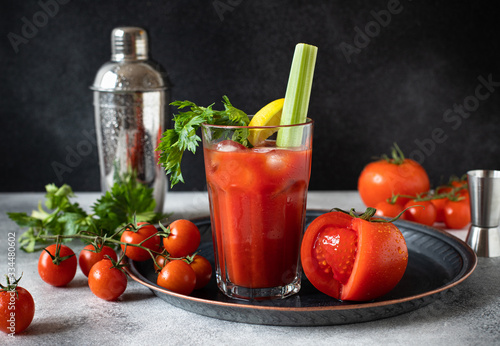 Classic alcoholic cocktail Bloody Mary with ice, lemon and celery. Cocktail ingredients and bar tools on a gray table and black background photo