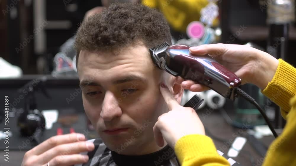 the guy from the barbershop.Women's hands trim the curly hair of a young man with a trimmer the guy from the barbershop.Women's hands trim the curly hair of a young man with a trimmer