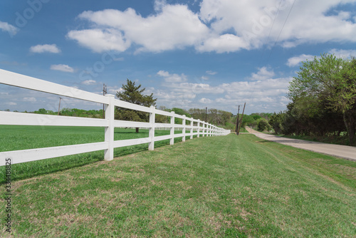 Scenic country road along long white fence leads to horizontal in cloud blue sky in Ennis, Texas, USA