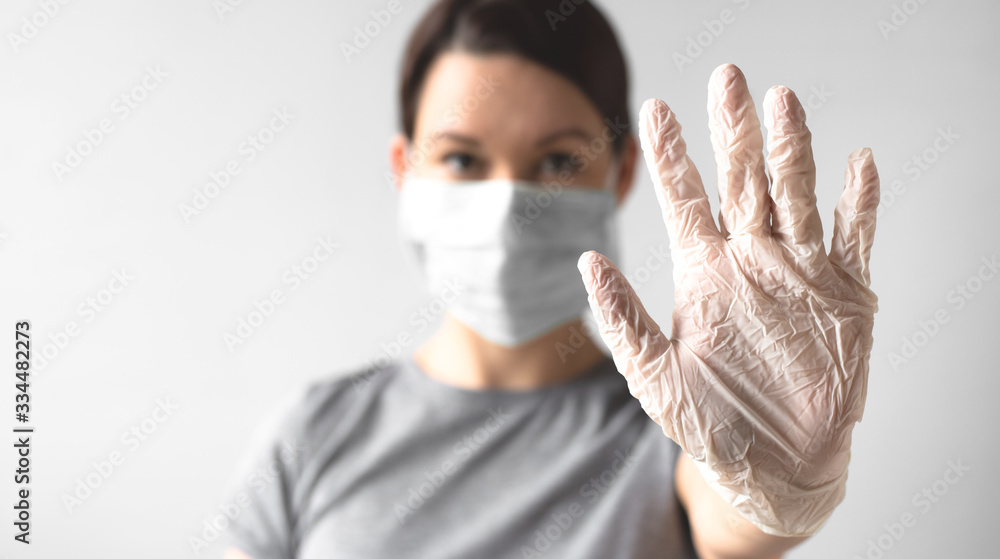 Coronavirus concept. Girl wearing a protective medical mask shows a gesture stop. Hand in a medical sterile glove. Protect your health. Stop the virus and pandemic covid-19 Coronavirus concept. Girl wearing a protective medical mask shows a gesture stop. Hand in a medical sterile glove. Protect your health. Stop the virus and pandemic covid-19