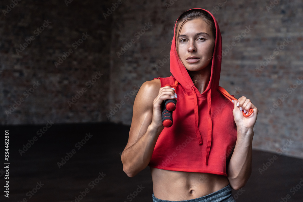 Fotografia do Stock: Attractive active young fit woman fitness trainer wear  read hood top stand in gym indoor hold jumping skipping rope look at  camera, cardio sport workout training lifestyle concept background