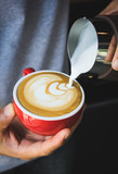 Barista pouring milk from pitcher making coffee latte art