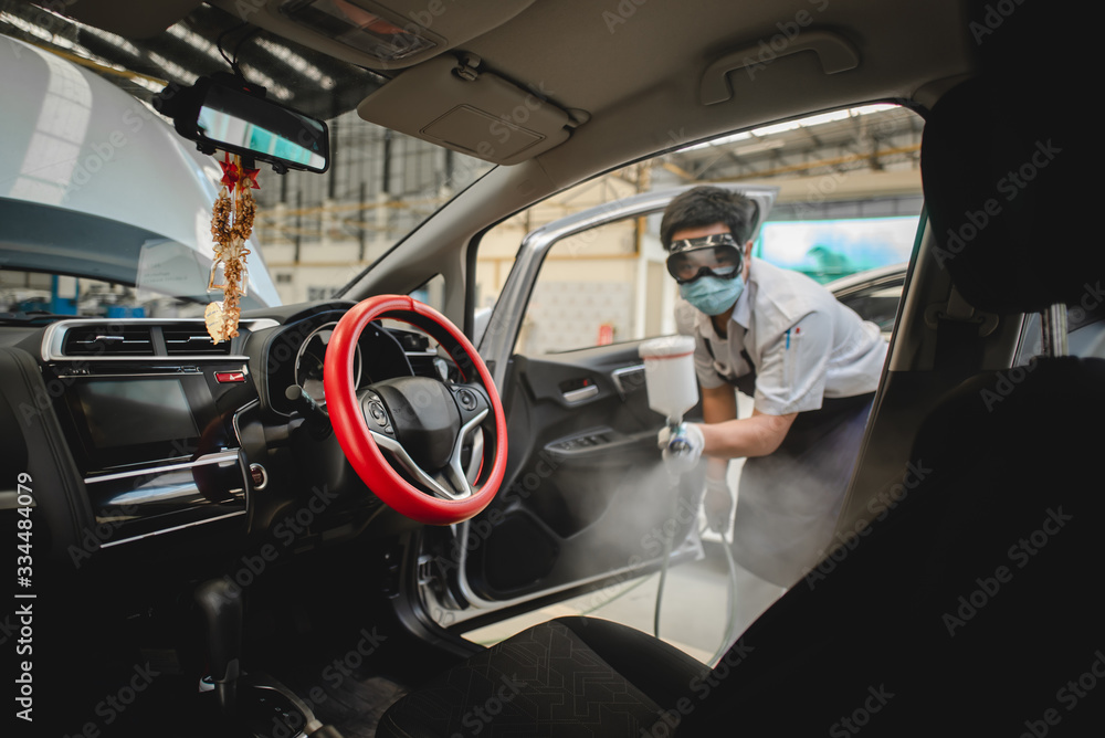 Mechanic spraying to kill the Covid-19 in the car that can kill the virus in the car. Mechanic wearing a protective mask and spraying aerosol or virus in the car.