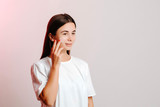 Beautiful young woman applying face cream on her cheek on grey background. Skin treatment concept. Face beauty routine.