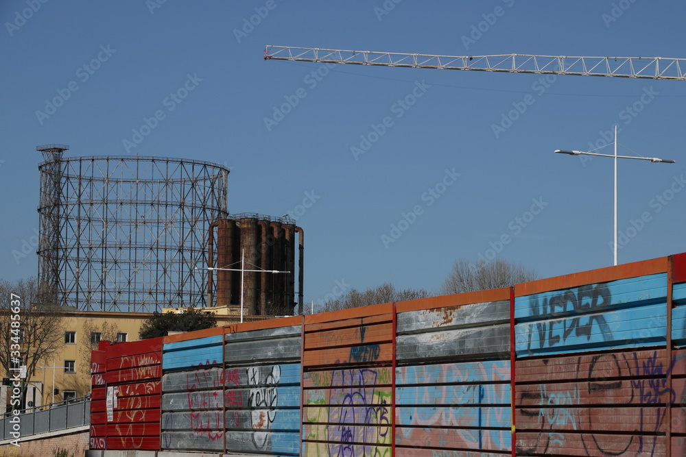 Garbatella district in Rome. Ancient gas meter and fence panels of a building site. Construction crane. Garbatella district in Rome. Ancient gas meter and fence panels of a building site. Construction crane.