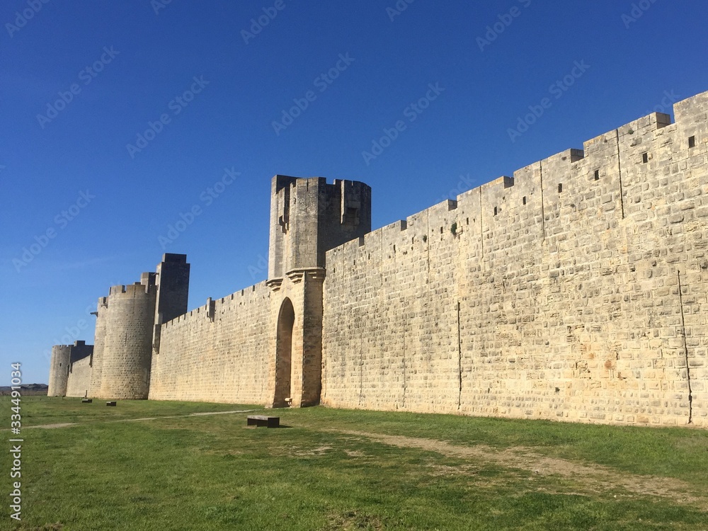 outside ancient medieval wall, in a bright light with blue sky and green grass, walled french city of Aigues Mortes