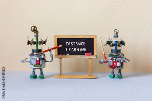 Distance learning and online education concept. Abstract interior classroom. Two funny teacher robots with a pencil and a pointer near the black chalkboard with handwritten text Distance Learning