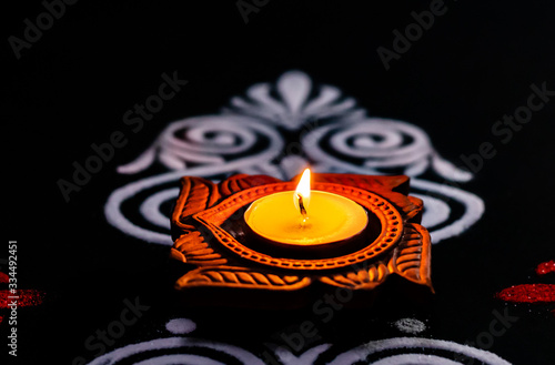 close up of glowing diya and white red rangoli on black background. festival of lights or diwai concept