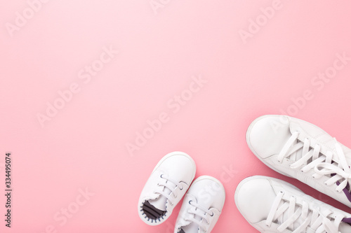 Mother and daughter white sport shoes on light pink table background. Pastel color. Empty place for text, quote or sayings. Closeup. Top down view.