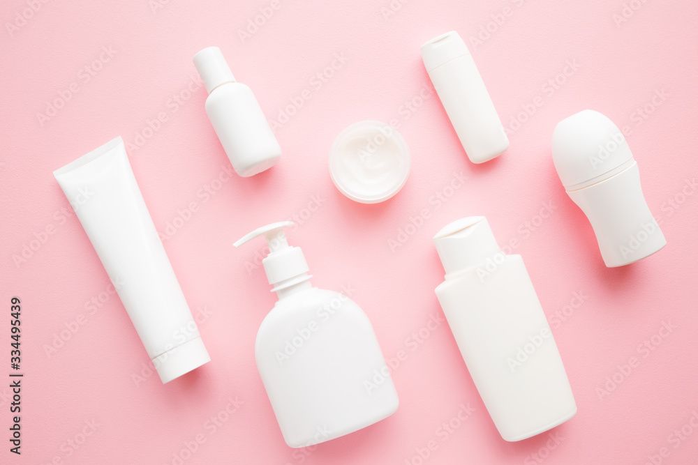 Different white toiletries on light pink table. Care about face, hands, legs and body skin. Women beauty products. Cosmetic pattern. Empty place for logo on bottles. Flat lay. Top down view. Different white toiletries on light pink table. Care about face, hands, legs and body skin. Women beauty products. Cosmetic pattern. Empty place for logo on bottles. Flat lay. Top down view.