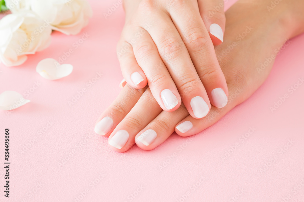 Young, perfect woman hands with white nails. Care about nails and clean, soft, smooth skin. Manicure, pedicure beauty salon. Beautiful roses on pastel pink table background. Fresh flowers. Closeup. Young, perfect woman hands with white nails. Care about nails and clean, soft, smooth skin. Manicure, pedicure beauty salon. Beautiful roses on pastel pink table background. Fresh flowers. Closeup.