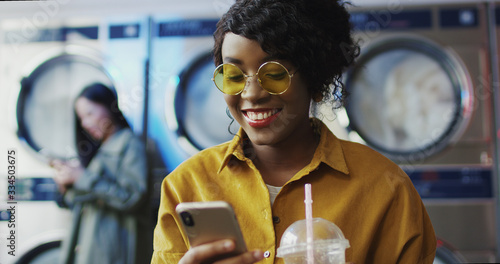 Slika na platnu African American girl drinking orange juice with straw, texting message on phone