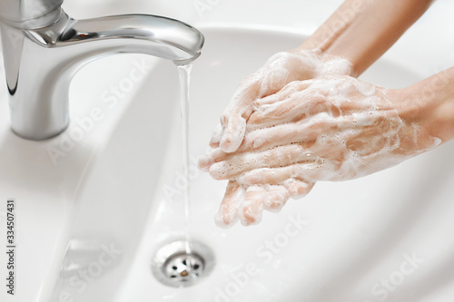 Hand Washing in white sink. Water flows from a faucet at soapy female hands. Covid-19 coronavirus protective measure.
