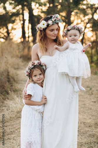 Happy elegant mother and her two beautiful daughters with flower wreaths in a nature at sunset © anatoliycherkas