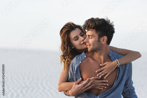 smiling passionate young woman touching boyfriend torso on beach