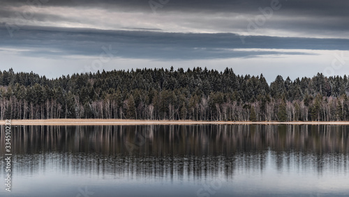 Landscape of a specular reflection in the lake, a dry grass, a cane and snags in the foreground, mountains and the forest on a background, ice on water, grass is covered with hoarfrost, tranquillity