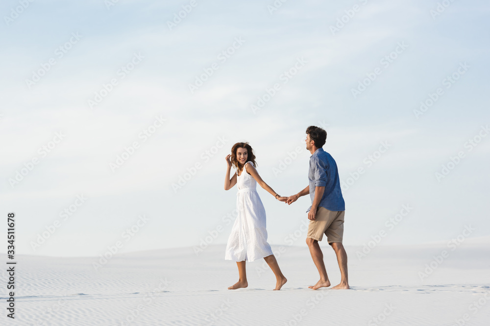 young couple walking on sandy beach and holding hands against blue sky young couple walking on sandy beach and holding hands against blue sky