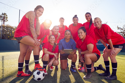 Portrait Of Coach Holding Digital Tablet With Womens Football Team Training For Soccer Match 