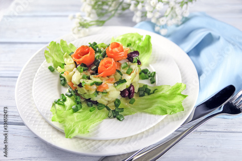 Salmon salad with fresh cucumber, red beans on lettuce leaves, served on a white porcelain plate. On a light wooden background with cutlery. Close-up