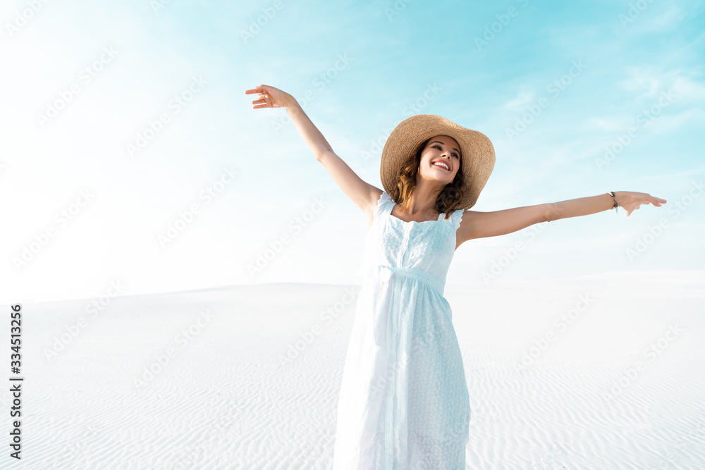 happy beautiful girl in white dress and straw hat with outstretched hands on sandy beach with blue sky happy beautiful girl in white dress and straw hat with outstretched hands on sandy beach with blue sky