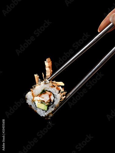 Japanese and Asian cuisine sushi rollin Chinese chopsticks with fresh ingredients over black