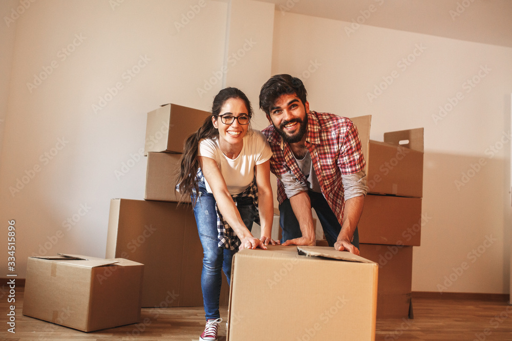 Young couple pushing big cardboard full of home essentials into a new home.Moving house. Young couple pushing big cardboard full of home essentials into a new home.Moving house.