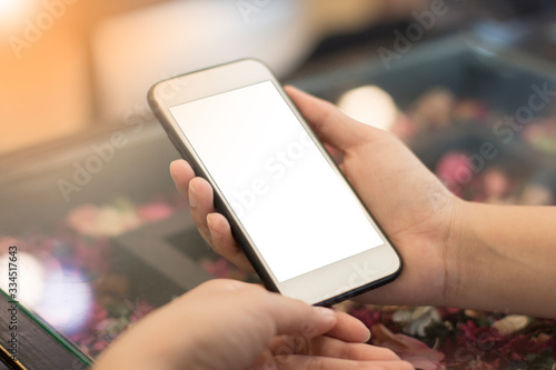Mockup image of a man's hand holding white mobile phone with blank black desktop screen on thigh in cafe