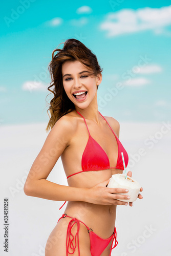 smiling beautiful sexy girl in swimsuit on beach with coconut drink