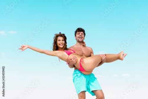 low angle view of young man holding beautiful sexy girlfriend in arms on sandy beach