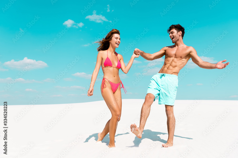 happy young couple holding hands on sandy beach