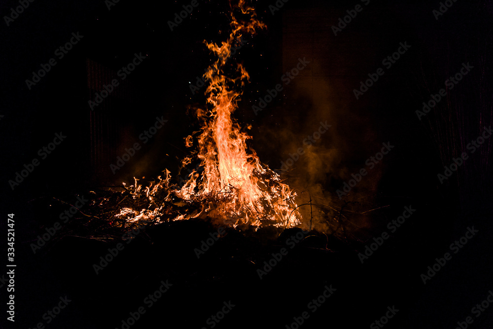 Bonfire on the street, burning branches and a tree, flame and sparks rise up.