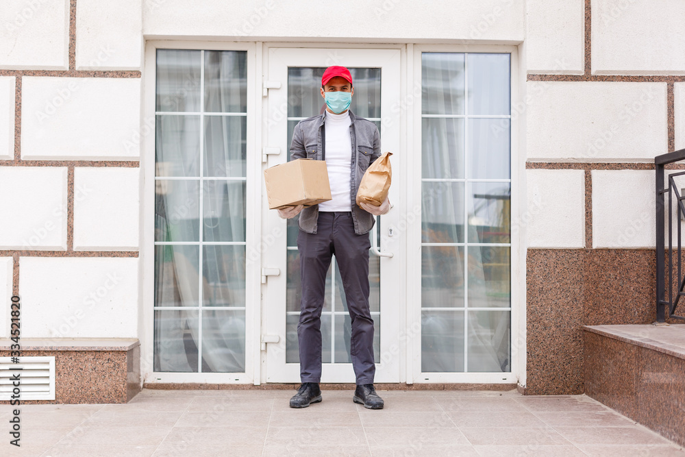 Courier in protective mask and medical gloves delivers takeaway food. Delivery service under quarantine, disease outbreak, coronavirus covid-19 pandemic conditions.