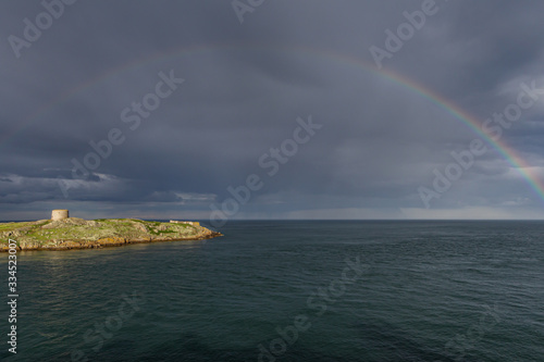 Blick vom Dillon’s Park auf die kleine unbewohnte Insel Dalkey Island mit Martello-Turm und einem Regenbogen an der Ostküste Irlands
