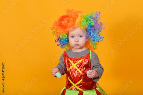 A small child  a girl in a clown wig  holds Easter eggs in her hands.