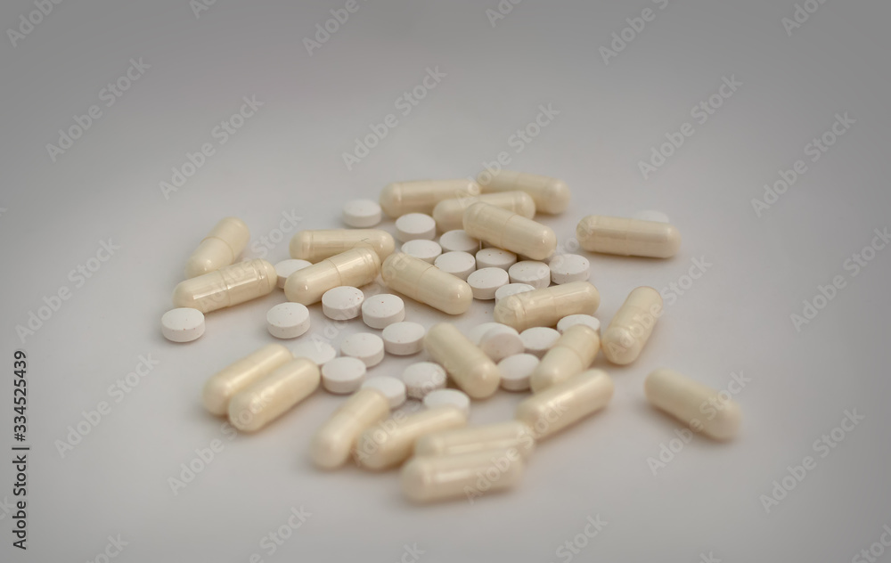 Bunch of pills - tablets and capsules - on white background. Selective focus. Light yellow capsules and white tablets are scattered over a white background. Virus cure.