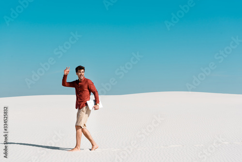 happy handsome freelancer on sandy beach with laptop against clear blue sky