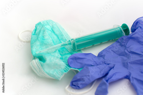 Used green disposable face mask, blue latex glove and plastic syringe lying on a white table. Typical surgical mask to cover the mouth and nose. Virus protection concept.