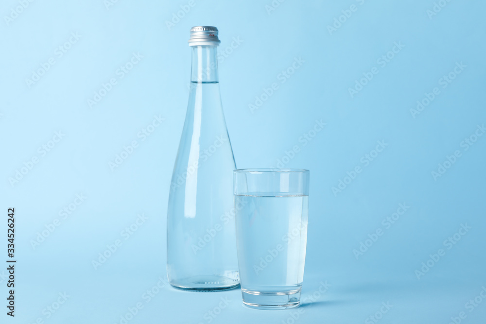 Glass and bottle with water on blue background, space for text Glass and bottle with water on blue background, space for text