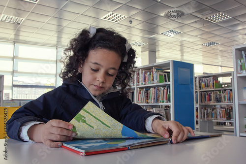 Niña leyendo un libro en la mesa de lectura.