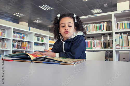 Niña leyendo un libro en la mesa de lectura.
