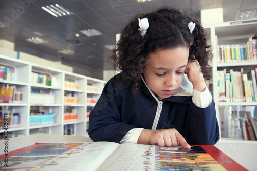Niña leyendo un libro en la mesa de lectura.