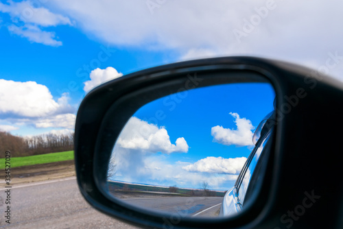 the blue sky with white clouds is reflected in the car mirror during the day . space for text.