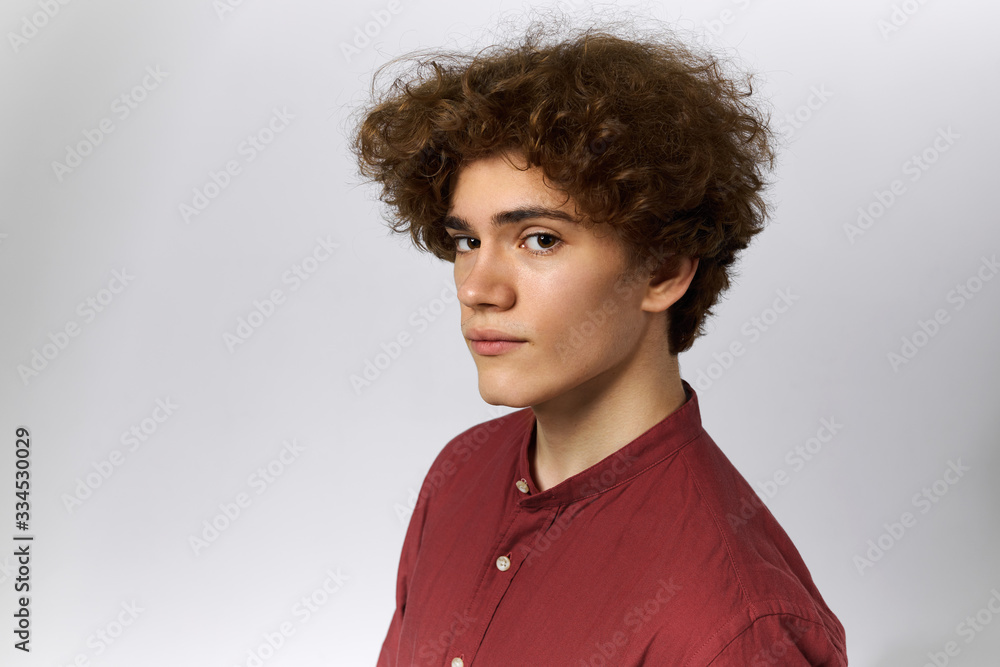 Obraz premium Half profile portrait of handsome young man wearing cotton casual shirt staring at camera with shy look posing isolated against blank gray studio wall background with copy space for your information