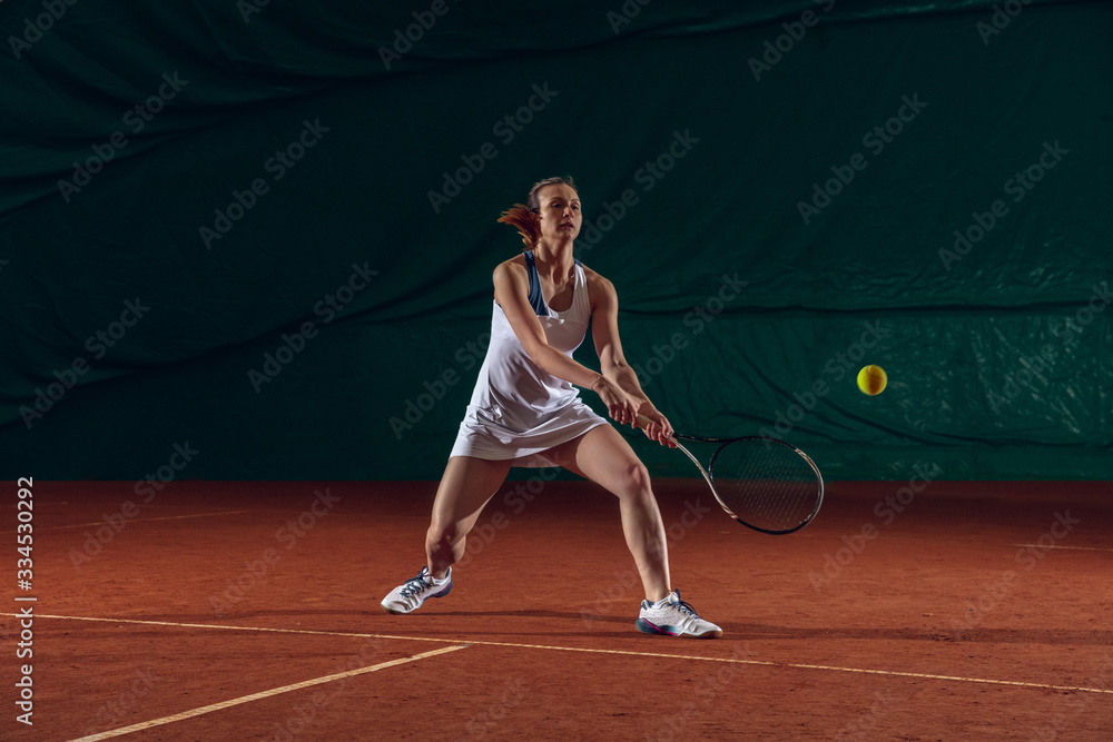 Young caucasian professional sportswoman playing tennis on sport court background. Training, practicing in motion, action. Power and energy. Movement, ad, sport, healthy lifestyle concept. Front view.